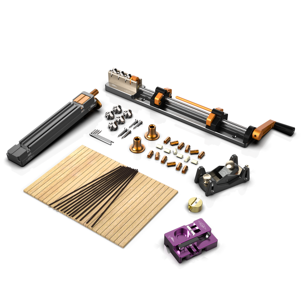 An array of pencil making tools and materials laid out on a table, including a plane sled unit, ferrule unit, and a variety of wooden pencil blanks.