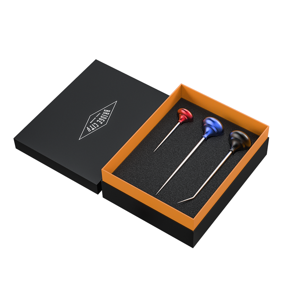 A set of three scratch awls with colored handles (red, blue, black) displayed in an open black box with an orange lining. The awls are tools used for precise hole layout and starting screws in woodworking.